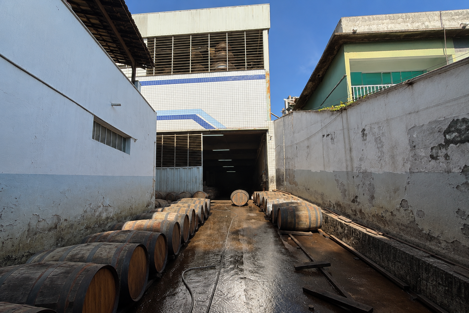 Corredor externo do galpão no Industrial 1, em Belo Horizonte, com fileiras de barris de carvalho e acesso coberto ao fundo