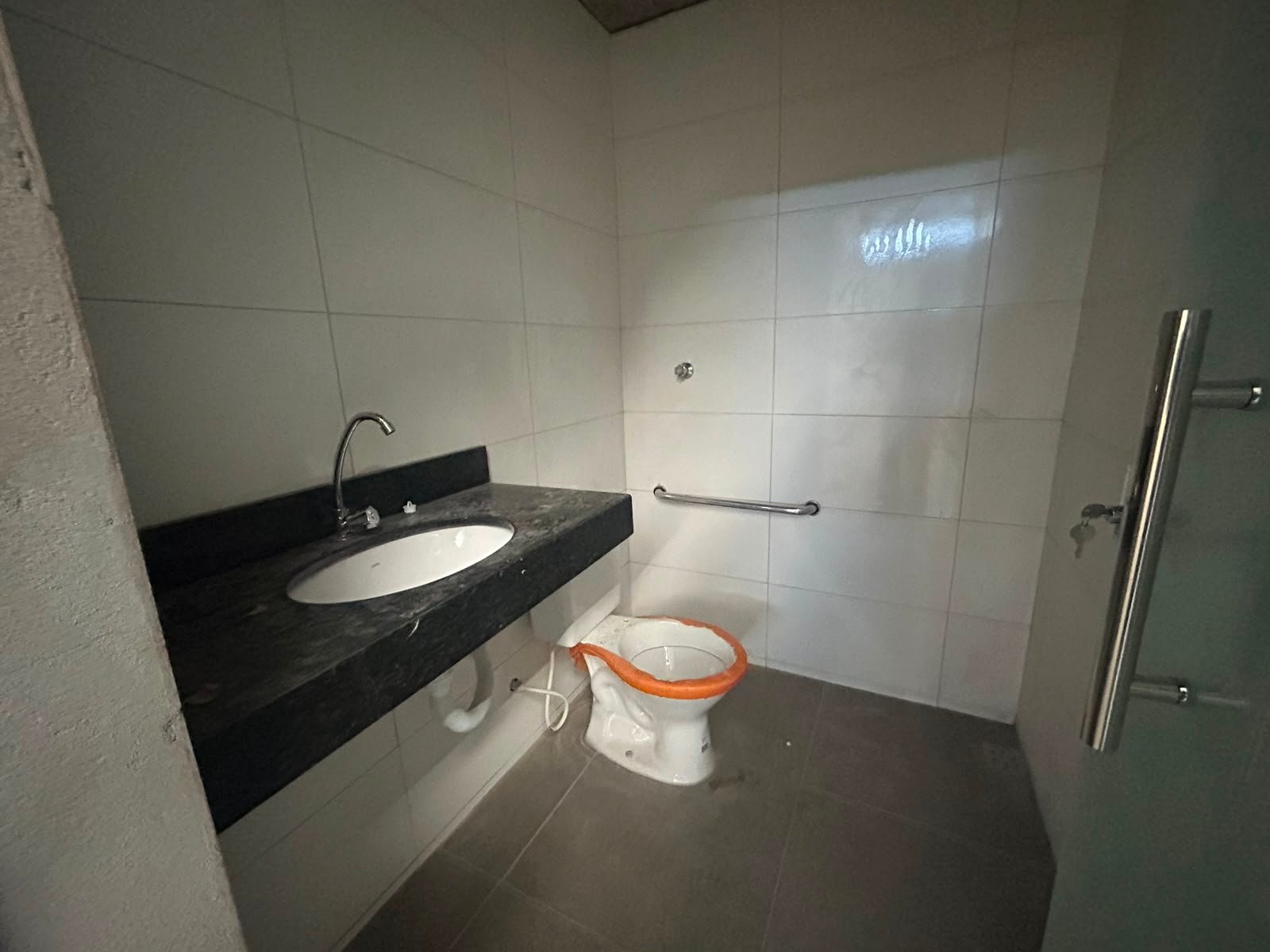Banheiro do escritório do galpão em Betim, revestido em porcelanato, com bancada de granito e barra de apoio
