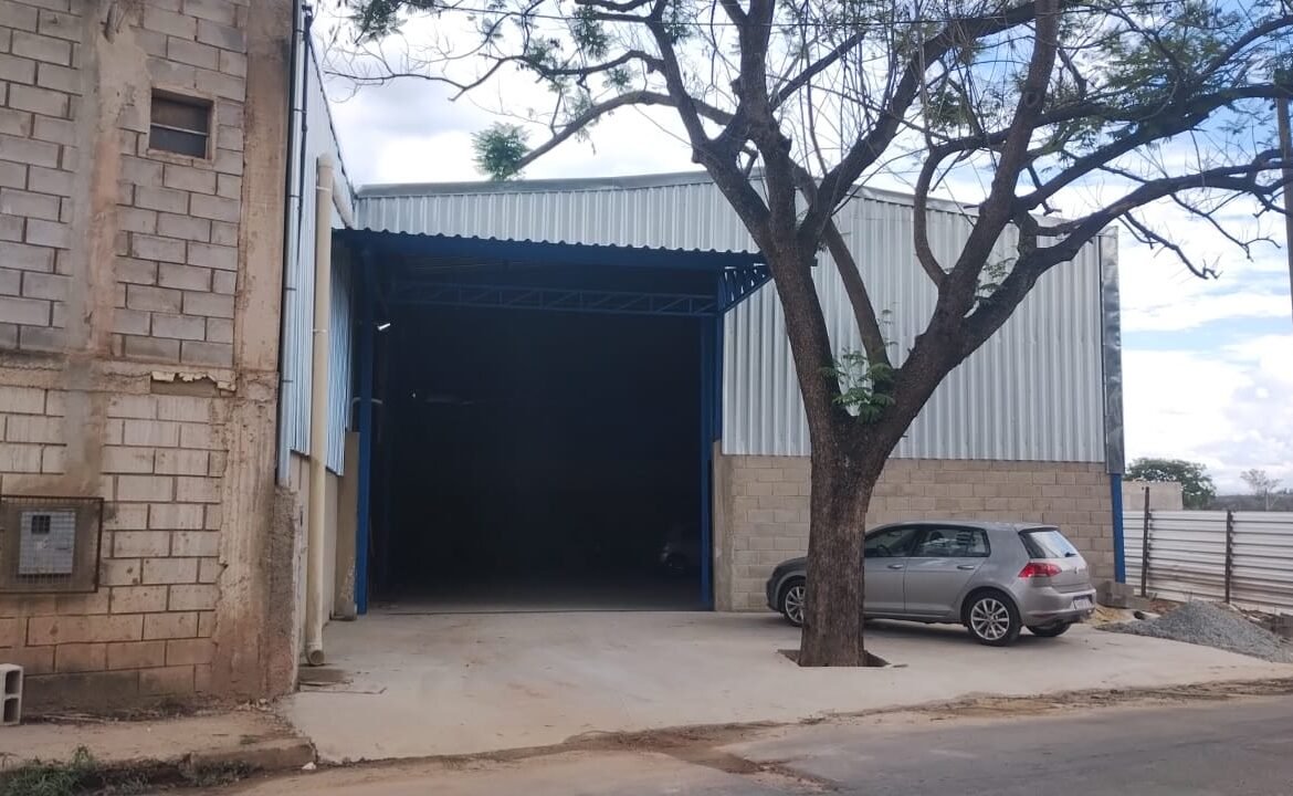 Portão de acesso do galpão no Arquipélago Verde, Betim Vista lateral da fachada do galpão em Betim/MG, com portão de acesso amplo e recuo pavimentado em frente ao imóvel