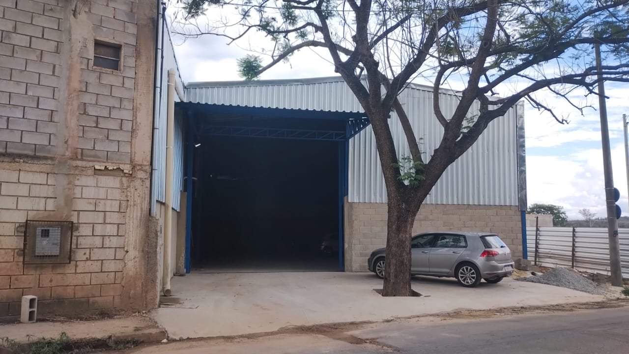Portão de acesso do galpão no Arquipélago Verde, Betim Vista lateral da fachada do galpão em Betim/MG, com portão de acesso amplo e recuo pavimentado em frente ao imóvel
