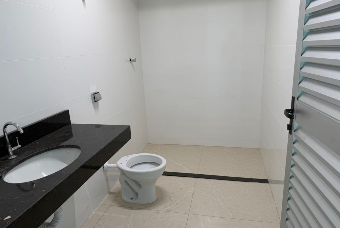 Banheiro do galpão no Riacho das Pedras, revestido em porcelanato branco, com bancada em granito preto