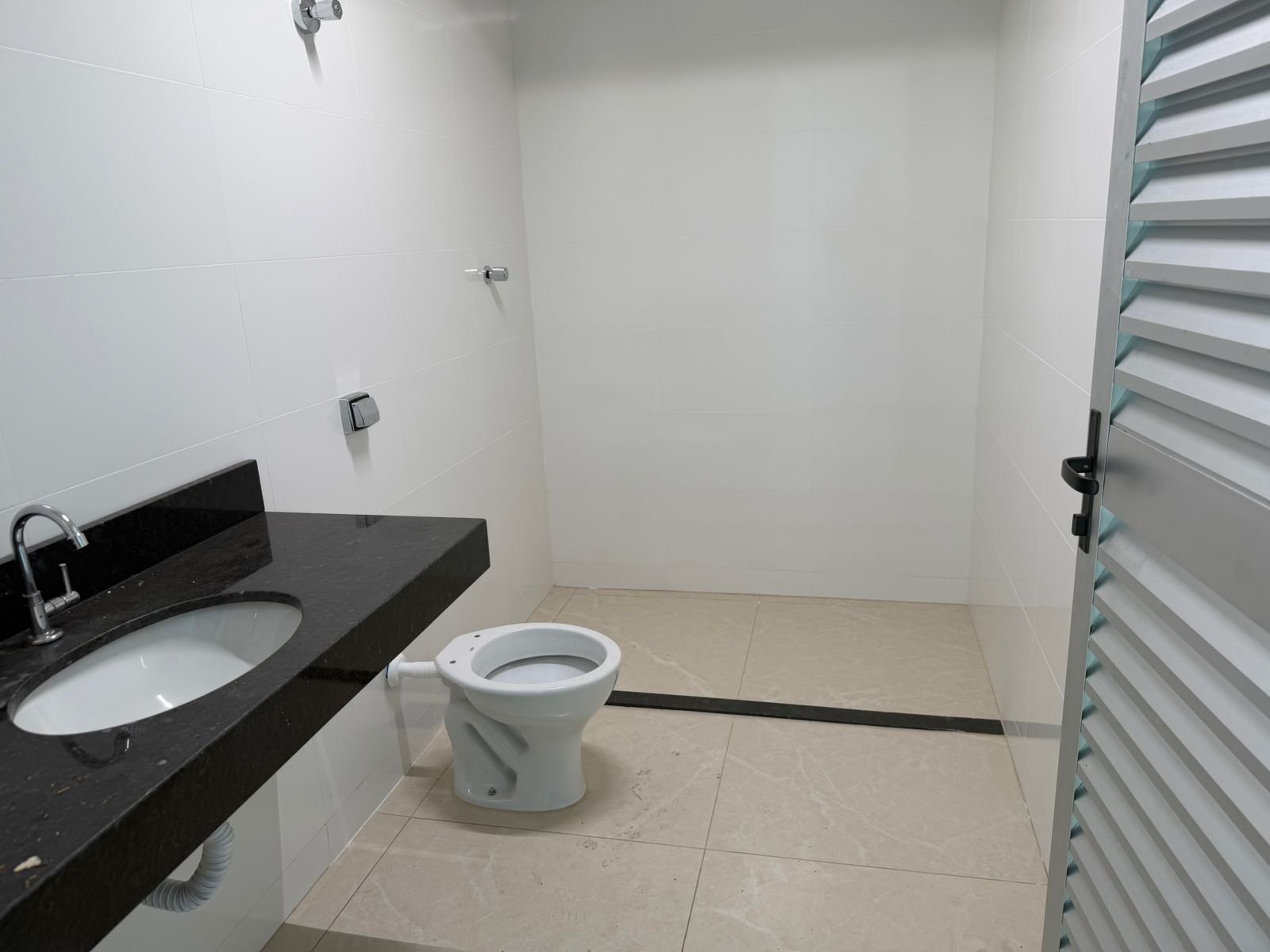 Banheiro do galpão no Riacho das Pedras, revestido em porcelanato branco, com bancada em granito preto